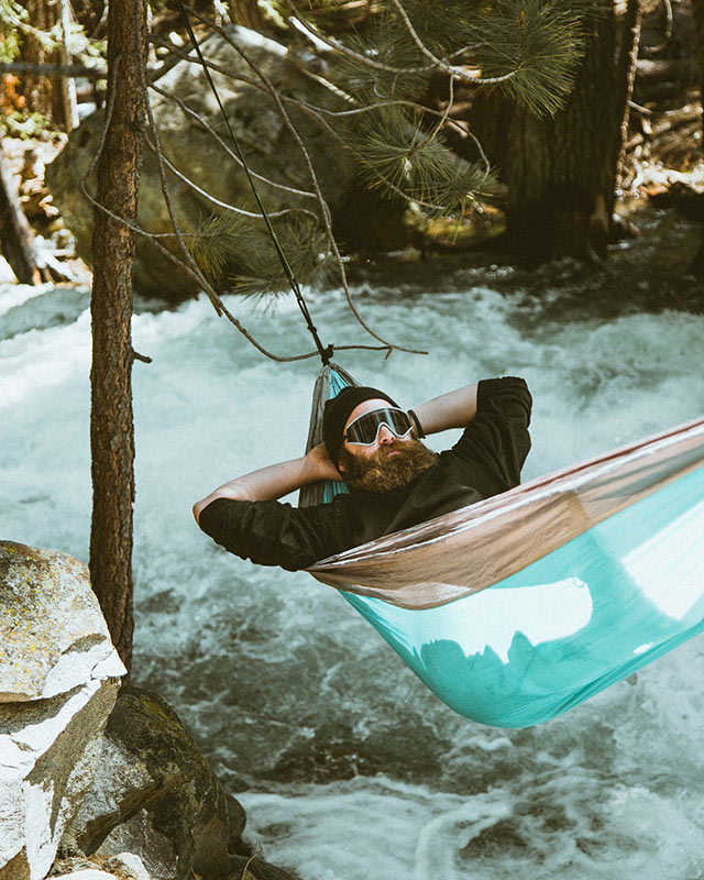 Man resting in a hammock over river stream